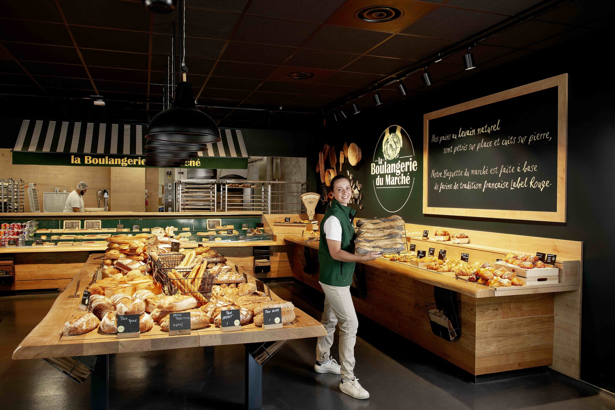 Une employée souriante avec une pile de pains frais à la Boulangerie du Marché.